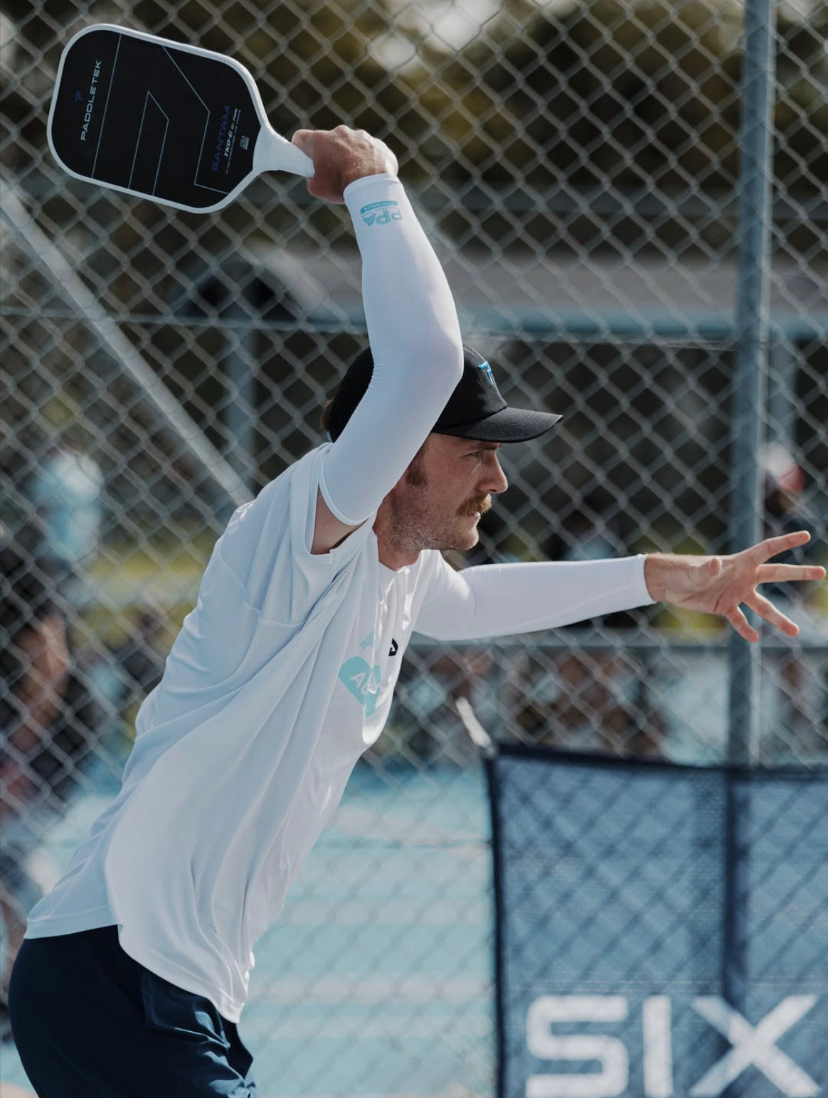 Person playing pickleball on a court wearing SParms Arm Sleeves